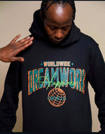 Load image into Gallery viewer, A person wearing a black hoodie with colorful text that reads WORLDWIDE DREAMWORK HAPPENS and a globe design on the front. Another hand is visible reaching towards the hoodie, highlighting the clothing.
