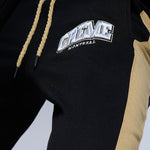 Load image into Gallery viewer, Close-up of a black sweatsuit featuring a bold CREME MONTREAL logo embroidered on the fabric. The clothing has gold-colored side stripes and drawstrings, adding a stylish contrast.
