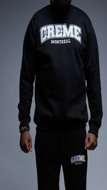 Load image into Gallery viewer, A man is wearing a black sweatsuit featuring the bold CREME MONTREAL logo on both the sweatshirt and pants. The clothing design is simple and sleek, with the logo prominently displayed.
