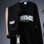 Load image into Gallery viewer, A black sweatsuit with the word CREME MONTREAL embroidered in bold white and gold letters on the top. The pants feature a contrasting gold stripe with a golden cord drawstring, hanging on a hanger. Perfect for stylish streetwear clothing.
