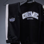 Load image into Gallery viewer, A black sweatshirt and sweatpants set hang on a rack, featuring the bold CREME MONTREAL logo in white lettering. The clothing has a contrasting white stripe on the pants, adding a sleek touch.
