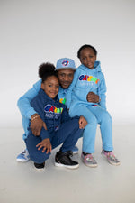 Load image into Gallery viewer, A man wearing a light blue hoodie and cap sits with two children dressed in colorful hoodies, one in dark blue and the other in light blue. They smile while posing together, showcasing stylish kids clothing.
