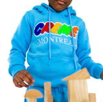 Load image into Gallery viewer, A child wearing a bright blue hoodie with colorful CREME MONTREAL embroidery is playing with wooden blocks. The clothing features a relaxed fit and visible drawstrings, perfect for kids.
